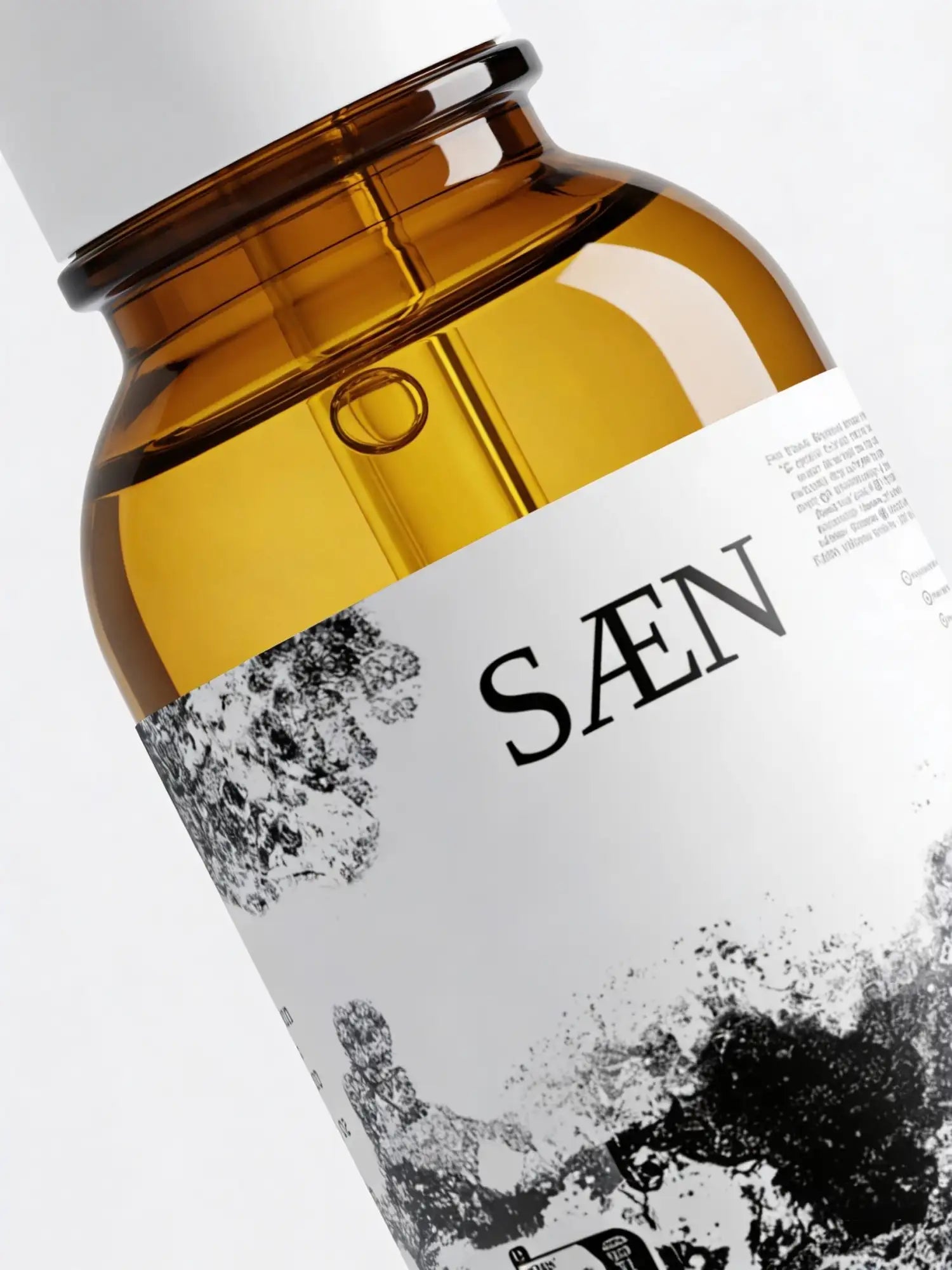 A sleek amber glass bottle with a white cap and label featuring the brand name ’saen’ in bold black letters, accented by abstract black-and-white splatter artwork.