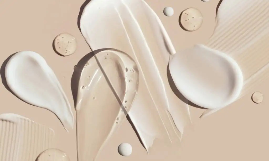 Swirls of creamy beige and white foundation, serum, or moisturizer spread across a soft tan surface.